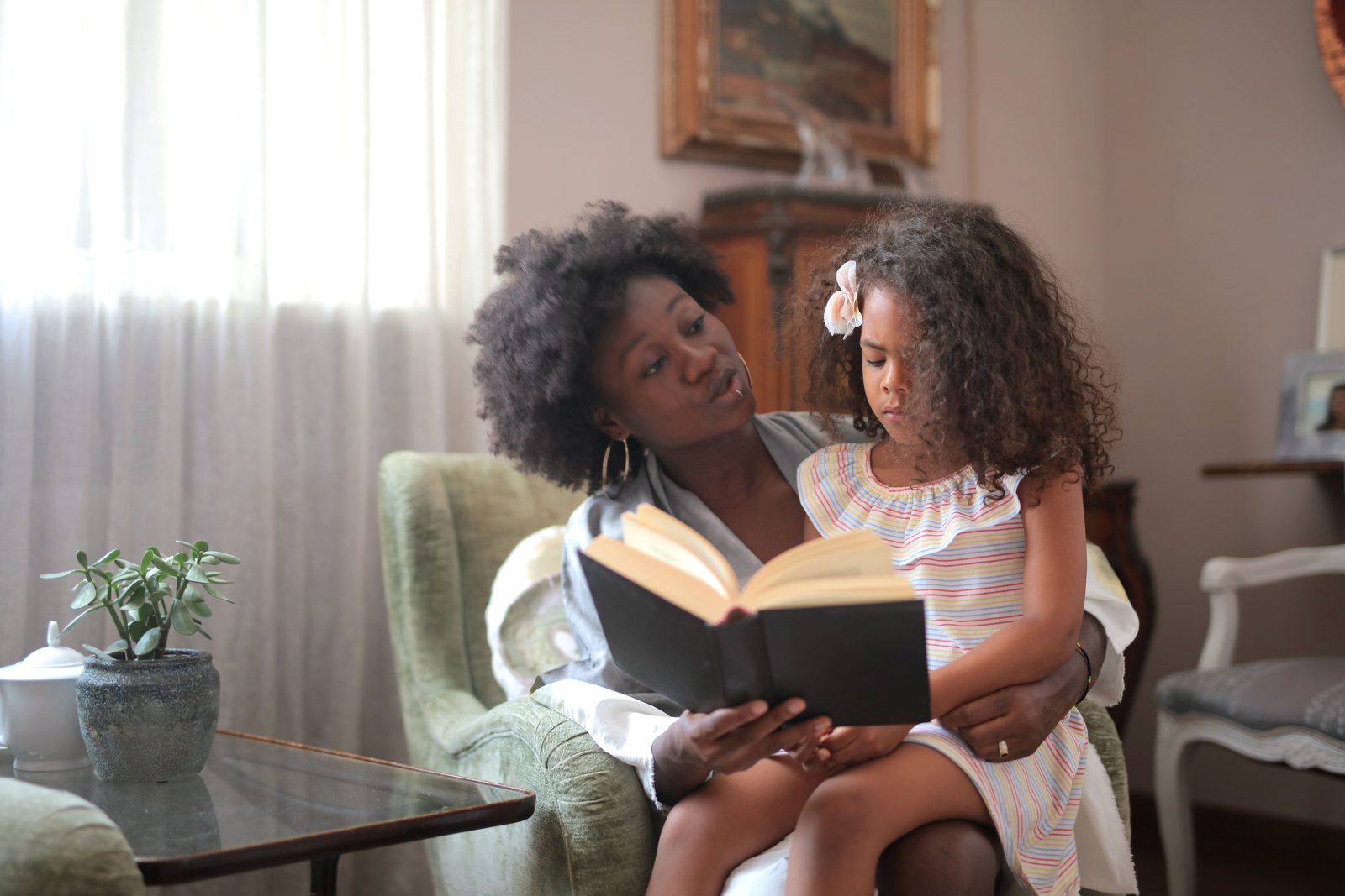 A caregiver reading a storybook with a young child settled on her lap in a warm, softly lit living room.